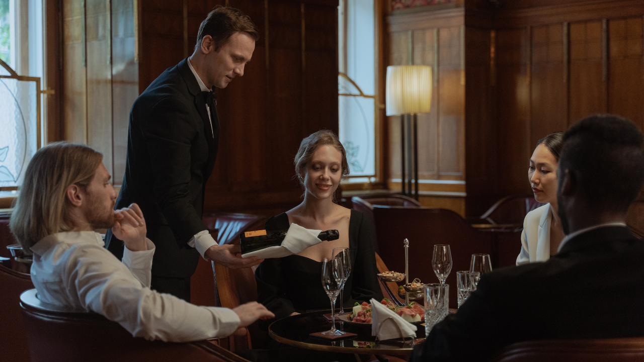 Why do waiters keep one hand behind their back when pouring wine?